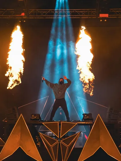 Alan Walker stands on a custom-built, geometric stage flanked by pillars of fire, creating a powerful and intense visual spectacle.