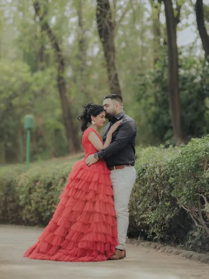 A classic portrait from an engagement shoot in a lush Pune garden. The woman's striking red gown and the couple's confident pose create a timeless and elegant image, showcasing a more formal and styled approach to pre-wedding photography.