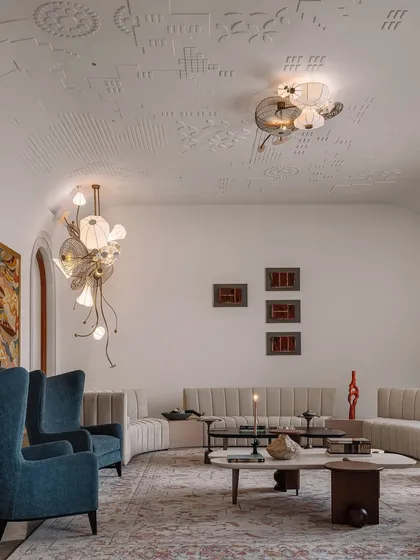 The ceiling of this formal living room is adorned with jewel-like light fixtures that resemble blooming flowers. These intricate, sculptural lights create a canopy of art, complementing the custom gypsum embroidery on the ceiling.