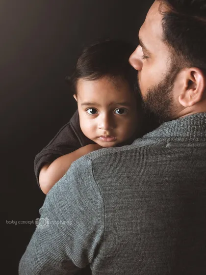 A tender moment captured from over the father's shoulder. The baby's direct gaze into the camera creates a powerful connection with the viewer, showcasing a quiet moment of trust and comfort.