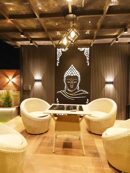 A close-up of the seating arrangement under the pergola, showing the intricate jaali panel and modern wicker chairs.