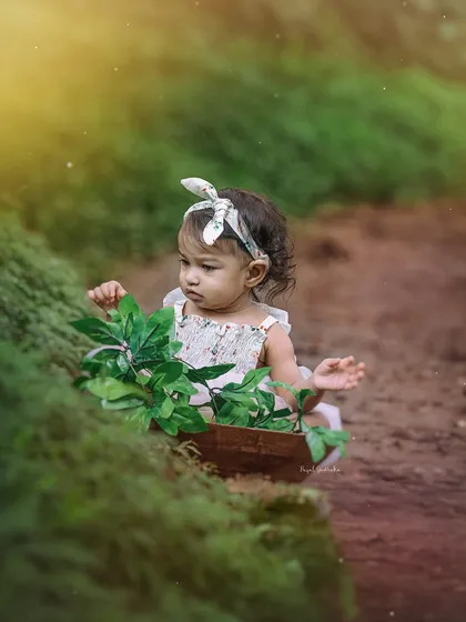 A pensive moment as a baby girl curiously examines the leaves in her basket, bathed in a soft, golden light.
