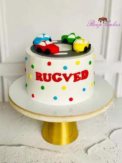 A colorful car-themed cake for a baby boy, with a racetrack on top and bright polka dots all around.