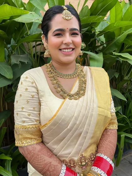 My radiant Malayalam bride glowing in a golden-white Mundu saree for her morning wedding. The makeup was clean and minimal, with flushed cheeks and a rosy pink lip to match the serene and happy occasion.