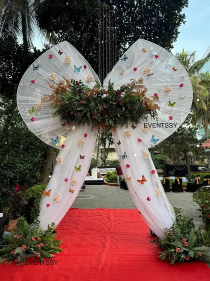 A grand entrance arch designed as a giant white bow adorned with flowers and butterflies. This whimsical and elegant entrance led guests down a red carpet into the main party area.