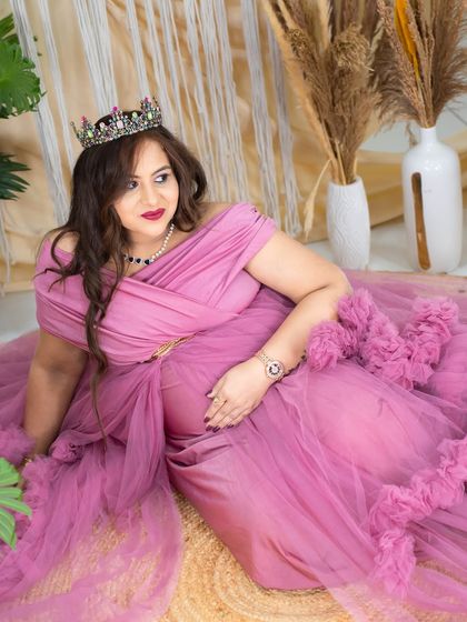 A moment of regal contemplation. The mom-to-be, in a dusty pink gown and crown, is seated on the floor of our boho studio, creating a relaxed yet elegant portrait.