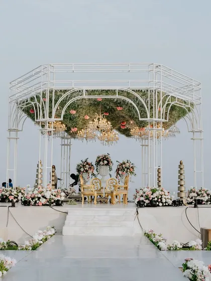 A full view of the seaside mandap, showing the elegant white structure, the lush floral arrangements in pastel hues, and the pristine white aisle leading to the ceremony space.