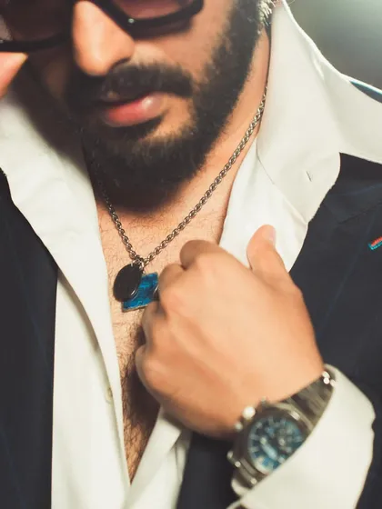 A close-up on the details of Arjun Kapoor's look. The open collar, layered necklaces, and the texture of the suit fabric come together to create a rich, layered aesthetic.
