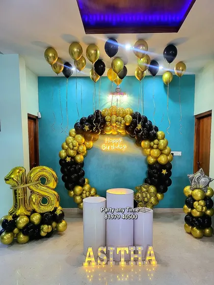 An 18th birthday celebration with a full ring of black and gold balloons. The setup includes a large '18' foil balloon arrangement, light-up letters, and helium balloons on the ceiling.