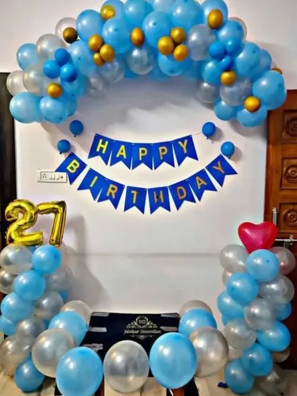 A simple and classic 27th birthday decoration at home. A blue and silver balloon arch is paired with a 'Happy Birthday' banner and foil number balloons.