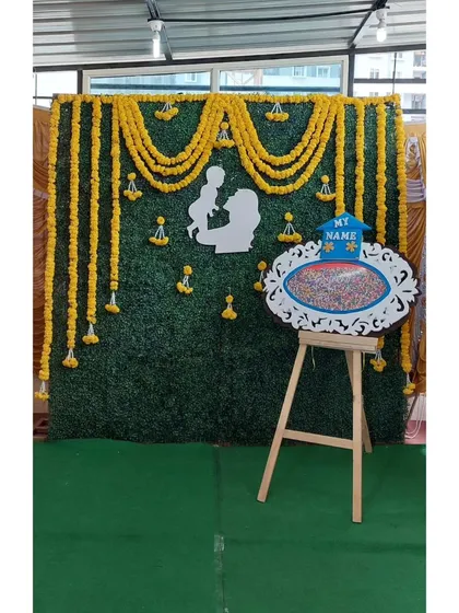 A closer look at our traditional green wall backdrop with marigold garlands. For this event, we also provided a decorative easel and board for a fun name-suggestion activity for the guests.