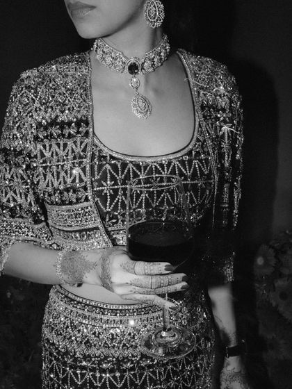 A detailed shot of the bride's stunning Sangeet outfit. The intricate embroidery and her relaxed pose with a glass of wine create a chic and sophisticated portrait.