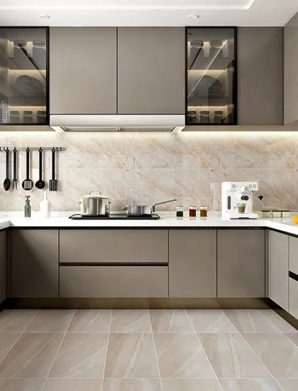 A sleek and minimalist kitchen with handleless taupe cabinets and built-in, glass-front display units with interior lighting. The design is unified by a marble-patterned backsplash and floor tiles, creating a clean and cohesive look.