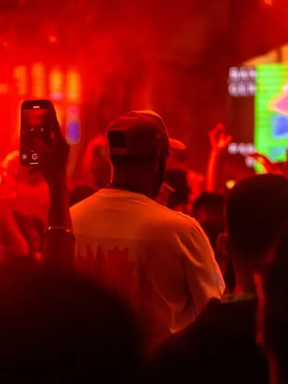 A shot from behind me in a red-lit club, with a fan holding up their phone to capture the moment.