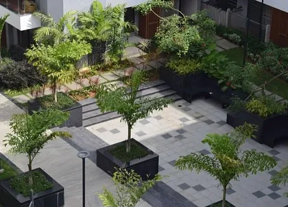 This high-angle view of the Sona Vistaas courtyard highlights the geometric interplay of paving, planters, and green lawns. The design provides a variety of textures and spaces, from open grass to shaded seating areas.