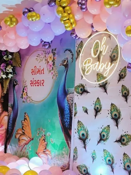 Another view of the Krishna themed baby shower, showing the 'Oh Baby' neon sign and the peacock feather details on the side panel.