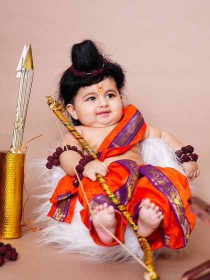 A divine portrait of a baby dressed as Bala Rama (young Lord Rama) with a bow and arrow for a festive photoshoot.
