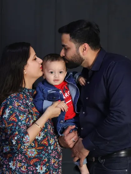 A tender moment between parents and their son. The father's kiss on the baby's head is a sweet, candid gesture that adds warmth to this classic studio portrait.