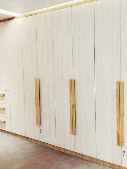 A modular wardrobe design featuring light-colored wood laminate shutters and distinctive long wooden handles. This unit also includes external drawers for easy access to frequently used items.