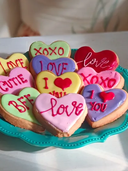 A colorful assortment of heart-shaped "conversation cookies" for Valentine's Day. Each cookie is hand-iced with classic messages like "Love," "XOXO," and "I ❤️ You."