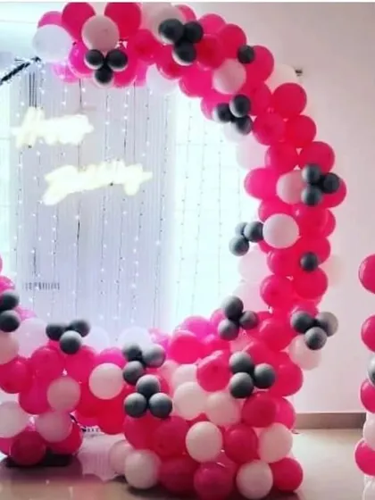 A full view of the circular balloon arch in pink, white, and grey. This modern frame, combined with a shimmer backdrop and neon sign, creates a perfect photo booth area for a first birthday.