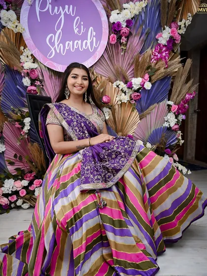 The bride looking radiant against a custom backdrop of purple and gold palm leaves, with a sign celebrating 'Piyu ki Shaadi'.