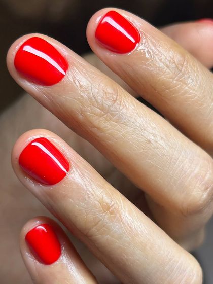 A vibrant, classic red manicure on short, natural nails. The high-gloss finish and precise application make this a standout look.