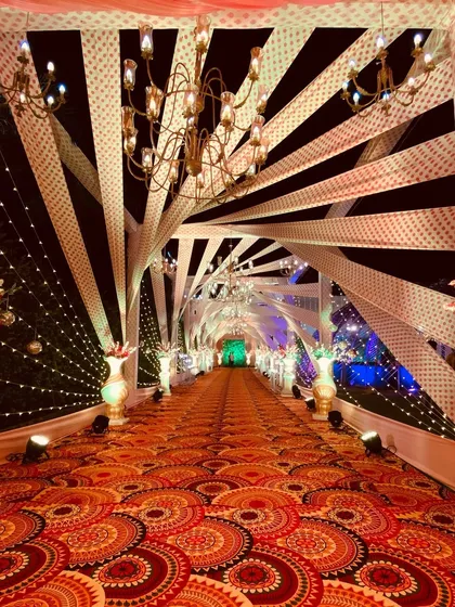 For this Sangeet entrance, I used a dynamic design with crisscrossing fabric strips and elegant chandeliers. The patterned carpet adds another layer of texture and visual interest.