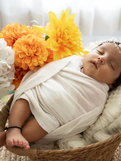 A close-up of a swaddled newborn in a basket, accented with bright yellow and white flowers. We use props and styling to complement your baby's innocence.