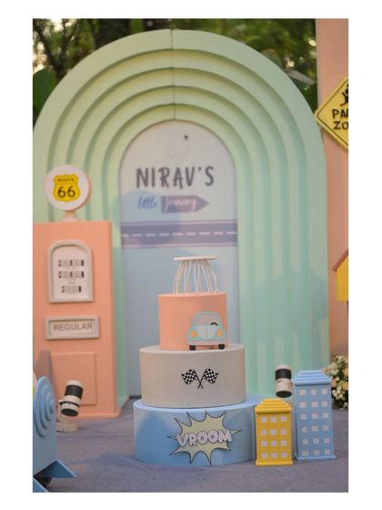 A close-up of the adorable car-themed cake, set against a pastel-colored, multi-layered arch backdrop.
