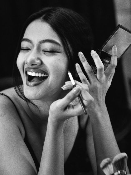 A burst of laughter during the makeup process. This candid black and white shot captures the fun and joy behind the scenes, showing a different side of the "getting ready" ritual.