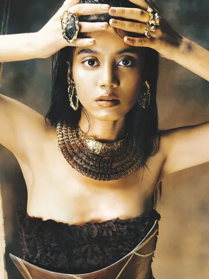A powerful close-up from this earthy, tribal-inspired shoot. The makeup is raw and bronzed, with a focus on glowing skin and intense eyes.