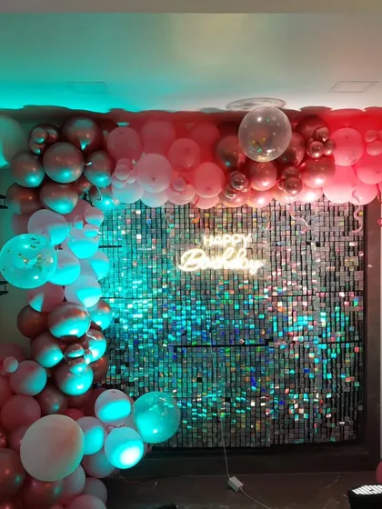 A movie night themed birthday party with a silver sequin wall, a "Happy Birthday" neon sign, and a colorful balloon garland.