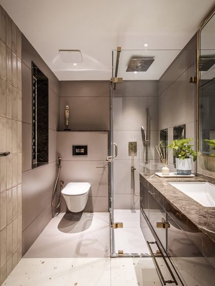 This guest bathroom features a sophisticated palette of grey tiles and rich brown marble for the vanity. A glass shower partition keeps the space feeling open, while brushed gold fixtures add a touch of understated luxury.