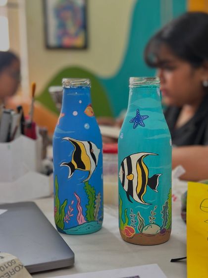 An order of underwater-themed bottles we painted for a client named Nithya. The vibrant blue background is adorned with colorful angelfish and sea plants.