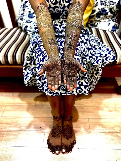 A full view of a bride showing off her beautifully stained mehendi on both hands and feet. The dark color signifies the deep love in a marriage and looks stunning in photos.
