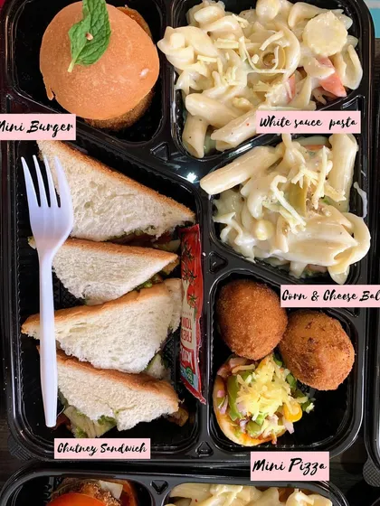A fun meal box perfect for kids and adults alike. It's packed with a mini burger, chutney sandwich, white sauce pasta, corn and cheese balls, and a mini pizza.
