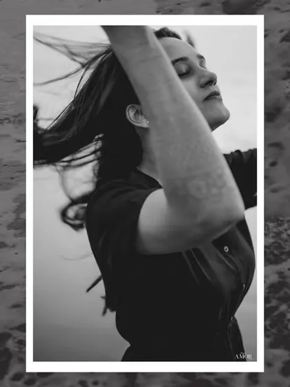 A black and white portrait of a woman with her eyes closed, hair blowing in the wind, set against the ocean waves. It's a moment of pure, uninhibited freedom.