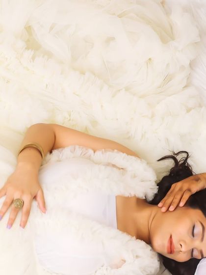 A serene close-up of a mother-to-be resting, enveloped in the soft ruffles of a white gown. This shot focuses on the peaceful and dreamy aspect of pregnancy.