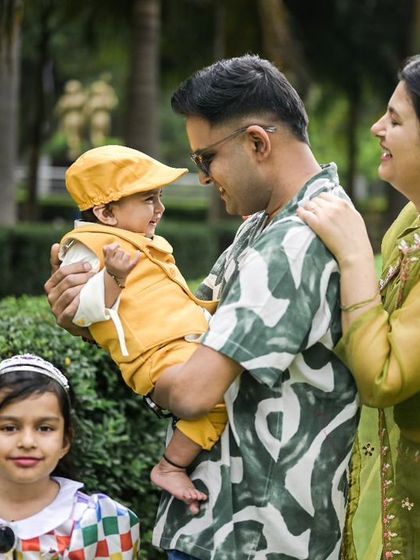 A happy family portrait taken outdoors. The father holds the baby, who is looking at him with a smile, while the mother and sister complete the lovely family group.
