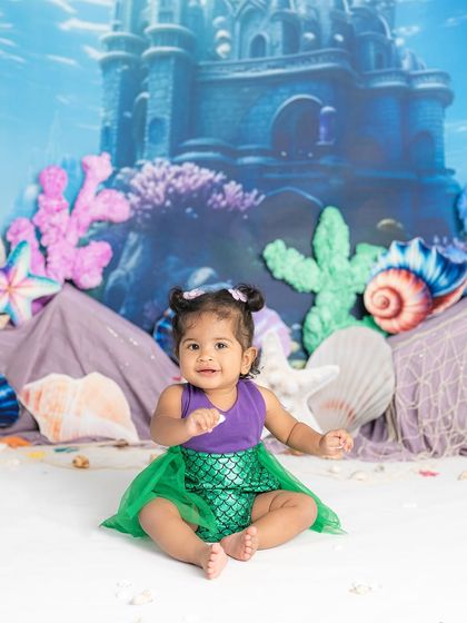 A sweet little mermaid sitting on the ocean floor. The underwater castle backdrop and colorful sea life props make this a truly magical scene.