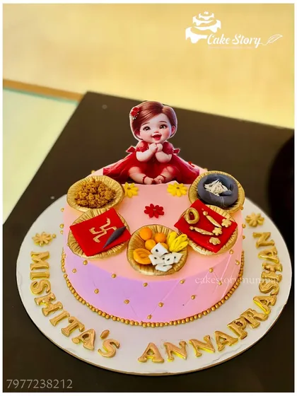 A beautiful cake for an 'Annaprashan' ceremony, celebrating a baby's first taste of solid food. The design includes traditional elements and a cute baby topper.