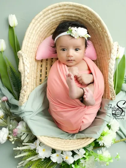 A beautiful portrait of an awake baby in a wicker basket, surrounded by soft fabrics and white tulips. The pastel color palette is soft and dreamy.
