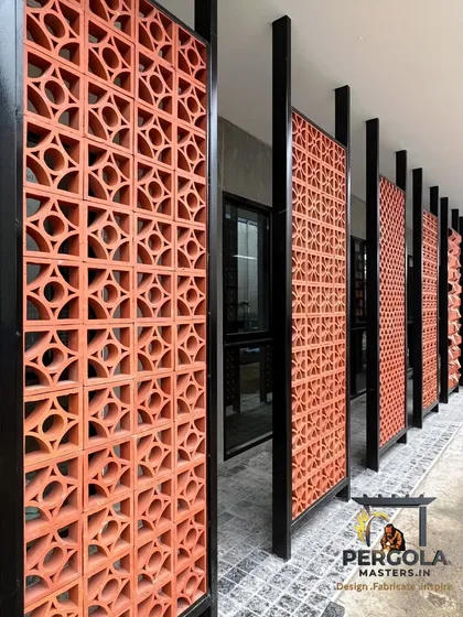 These terracotta jali brick panels, framed in black metal, create a visually striking and functional wall. The design allows for natural airflow and light while providing privacy, blending traditional materials with a modern aesthetic.