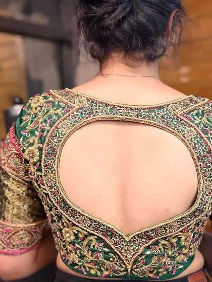 A unique heart-shaped open back design on a green bridal blouse. The entire piece is covered in detailed zardosi and threadwork, blending traditional craftsmanship with a modern silhouette.