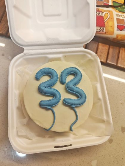 A close-up of a birthday bento cake in its takeaway box. The number "33" is piped to look like balloons, making it a fun and modern design.