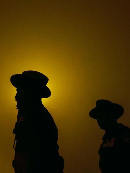 A silhouette of two officials against a hazy, yellow sky in New Delhi. The minimalist composition and warm glow create a cinematic and mysterious mood.