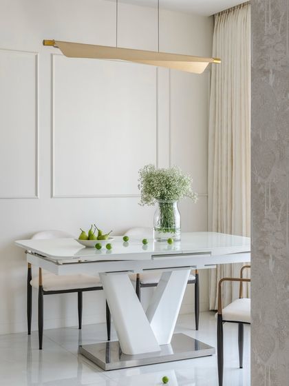 The dining area of the 'Soothing Antidote' home. The space is defined by its simplicity, with a modern table and a sculptural light fixture, allowing the subtle textures and clean forms to create a sense of peace.