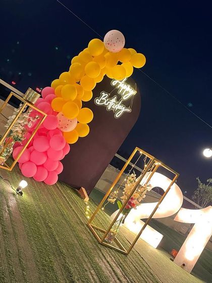 This is a duplicate of ID 21, 60, 67, 91, 121, 168, 206, 232, 239. A vibrant 21st birthday decoration on a rooftop. This setup features a balloon arrangement in hot pink and yellow, a 'Happy Birthday' neon sign, and large marquee numbers against a city skyline.