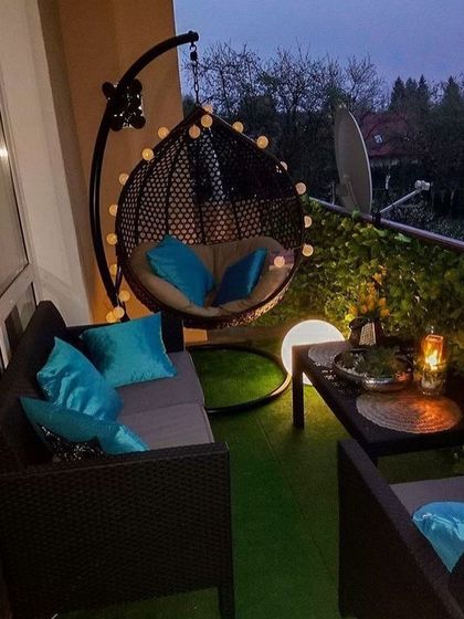 This setup proves you don't need a lot of space to create a comfortable outdoor lounge. A combination of a wicker sofa, a modern swing chair, and soft lighting makes this small balcony the perfect private spot to unwind.